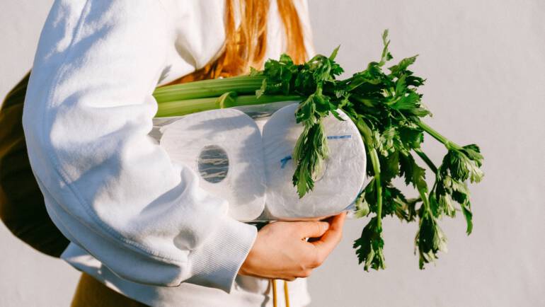 person carrying tissue rolls and vegetables